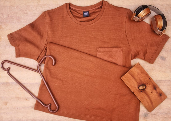 A product photograph by a UGC Creator of a brown t-shirt featuring  a pair of sunglasses, and a wooden hanger