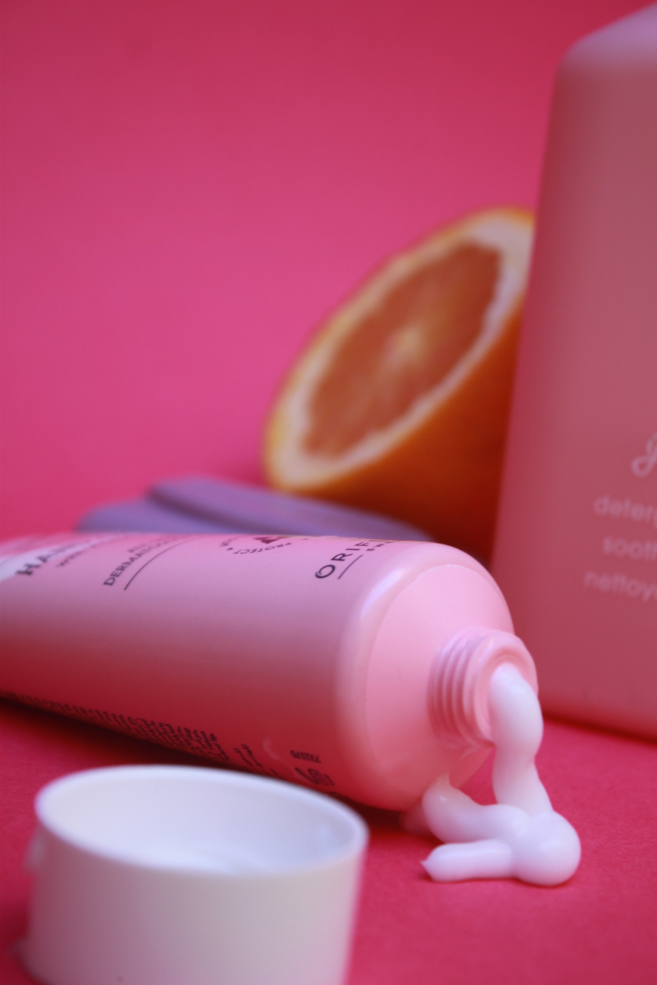 A product photograph by a UGC Creator of a bottle of the Glow Essentials Hand Cream with Vitamins E & B3 next to an orange slice